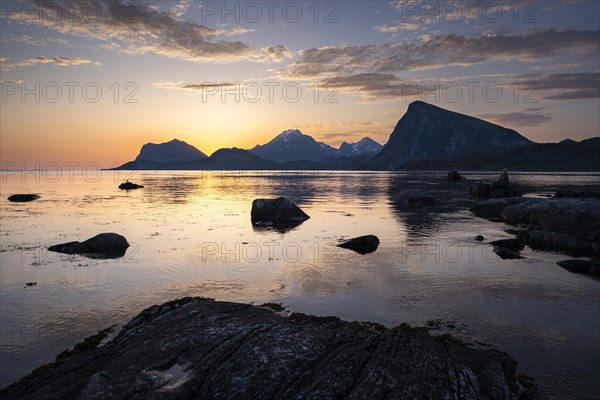 Landscape on the Lofoten Islands. View from Flakstadoya to Vestvagoya with the snow-covered mountain Himmeltindan and Offersoykammen to the right. The mountains are reflected in the sea. At night at the time of the midnight sun in good weather. Early summer. Lofoten, Norway, Europe