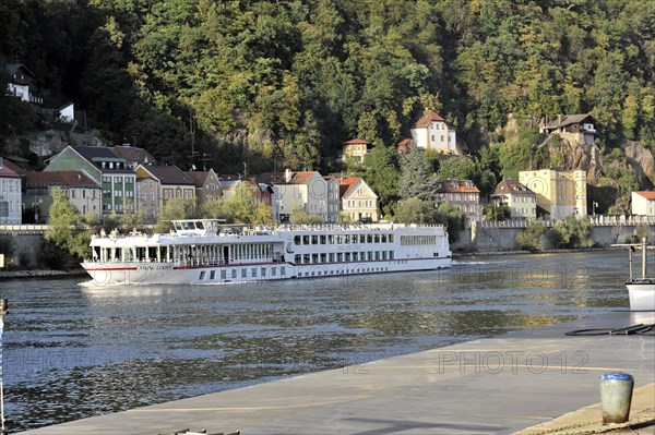 The river cruiser VIKING EUROPE, year of construction 2001, 114, 30m length near Passau, A river boat passes a row of picturesque houses standing between trees on a river bank, Passau, Bavaria, Germany, Europe