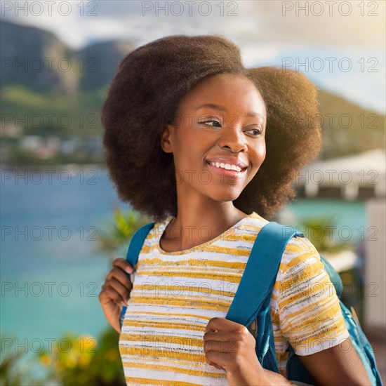 Cheerful woman with a backpack and afro hair in a striped shirt, basking in sunlight with a content expression, blurry moody landscaped background with bokeh effect, AI generated