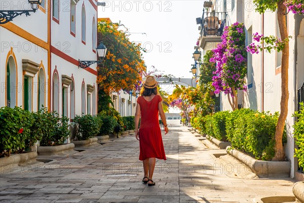 A woman walking in a red dress in the flower-filled port of Mogan town in the south of Gran Canaria. Spain