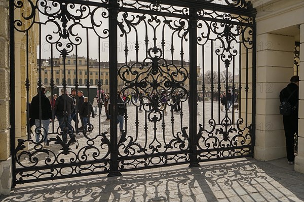 Through an ornate wrought iron gate you can see the forecourt of Schoenbrunn Palace in Vienna with passers-by