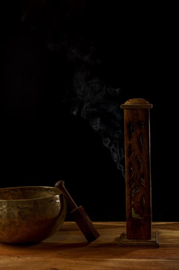 Tibetan singing bowl next to a wooden censer with smoke coming out isolated on black background with copy space
