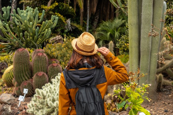 A woman wearing a straw hat walks through a desert garden. She is carrying a backpack and she is enjoying her time in the garden