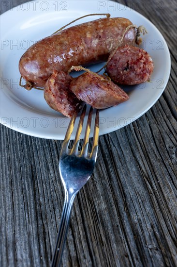 A Plate with Luganighe Sausage with a Fork on a Wood Table with Sunlight in Lugano, Ticino, Switzerland, Europe