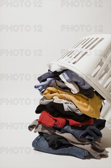 Close-up of white plastic laundry hamper or basket on top of pile of dirty clothes that includes blue jeans, underwear and t-shirts on white background, Studio Composition, Quebec, Canada, North America