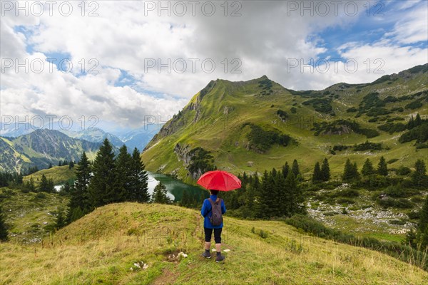 Woman 60-65 hiking with umbrella, behind her Seealpsee and Seekoepfel, 1919m, Allgaeu Alps, Allgaeu, Bavaria, Germany, Europe