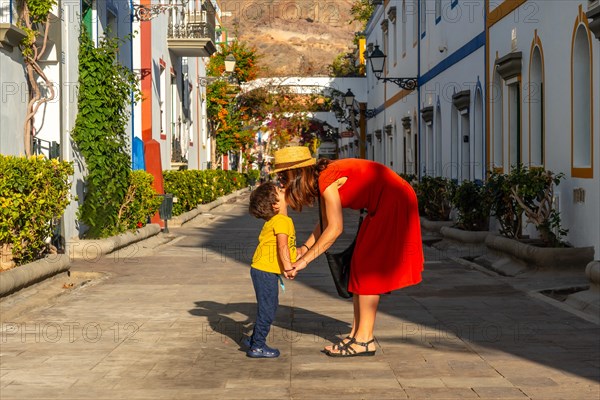 Mother in a red dress and her son walking in the port of the town Mogan in Gran Canaria. Family vacation