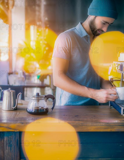 Man focuses while preparing a pour-over coffee with kettle on a wooden surface, yellow bokeh lights adorn the scene, Vertical aspect ratio, AI generated