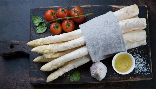 Bunch of white asparagus on a wooden board with tomatoes, garlic and oil, bunch of white asparagus wrapped in a damp kitchen towel, KI generated, AI generated