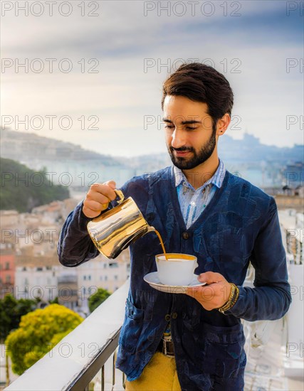 A casually elegant wealthy dressed man pours coffee on a balcony overlooking the city in the morning, Vertical aspect ratio, AI generated