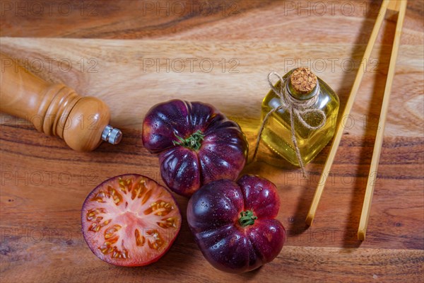 Top view of a group of tasty fresh tomatoes of the blue variety next to some wooden tongs, olive oil and a pepper shaker on a wooden table