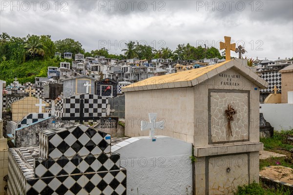 Famous cemetery, many mausoleums or large tombs decorated with tiles, often in black and white. Densely built buildings under a dramatic cloud cover Cimetiere de Morne-a-l'eau, Grand Terre, Guadeloupe, Caribbean, North America