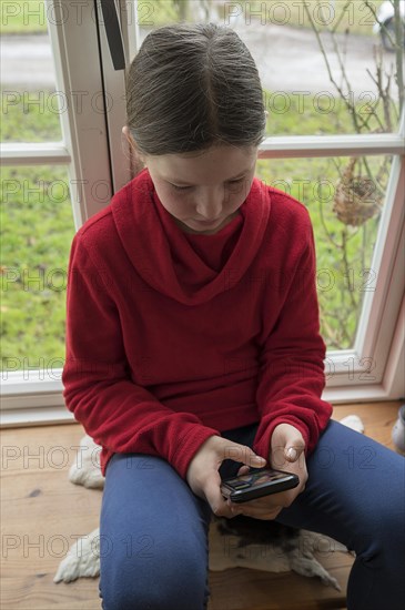 Girl, 10 years old, sitting on the windowsill with mobile phone, Mecklenburg-Vorpommern, Germany, Europe