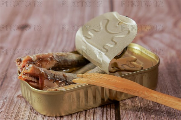 Tin can with tasty sprats with a wooden fork on a wooden table