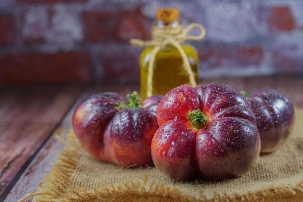 Group of tasty fresh tomatoes of the blue variety on a burlap cloth with a bottle of olive oil in the background