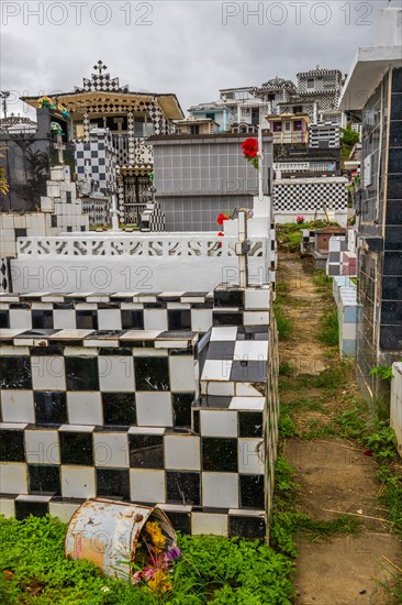 Famous cemetery, many mausoleums or large tombs decorated with tiles, often in black and white. Densely built buildings under a dramatic cloud cover Cimetiere de Morne-a-l'eau, Grand Terre, Guadeloupe, Caribbean, North America