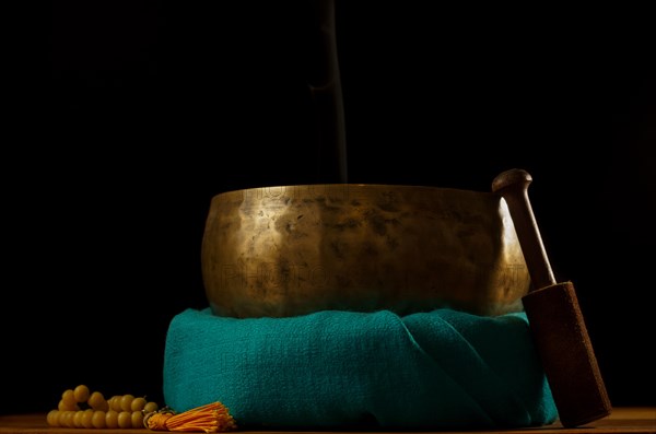 Tibetan singing bowl smoking on green cloth next to a Buddhist japa mala isolated on black background with copy space