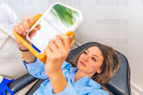 Adult caucasian woman lying on stretcher in a beautician clinic looking herself after apply hyaluronic acid injection on lips using a mirror