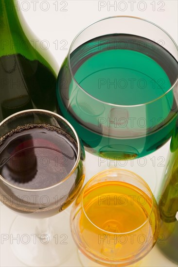 Close-up various size clear glass drinking glasses filled with assorted green, yellow and red alcoholic liquors on white background, Studio Composition, Quebec, Canada, North America