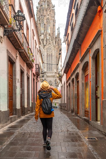 A tourist woman with a hat walking along a beautiful street next to the Church of San Juan Bautista, Arucas Cathedral, Gran Canaria, Spain, Europe