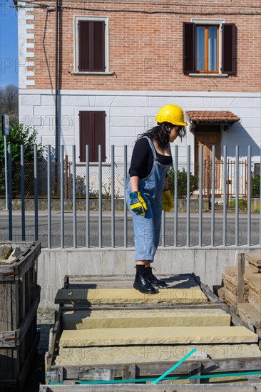 A woman in construction gear is standing by a fence, measuring something on a build site