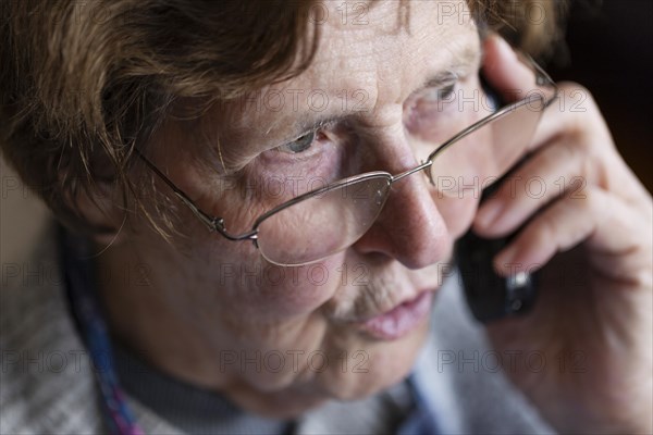 Senior citizen looks serious, frightened while talking on the phone in her living room, Cologne, North Rhine-Westphalia, Germany, Europe