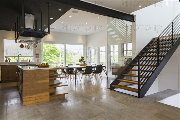Kitchen, dining room and American walnut wood and black powder coated cold rolled steel stairs inside modern cube style home, Quebec, Canada, North America