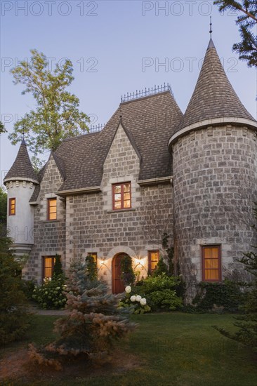 2006 reproduction of a 16th century grey stone and mortar Renaissance castle style residential home facade at dusk in summer, Quebec, Canada, North America