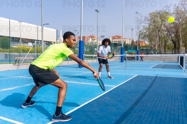 Side view full length photo of two african american young male friends having fun during pickleball match outdoors