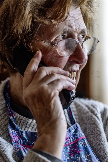 Laughing senior citizen with smock talking on the phone at home in her living room, Cologne, North Rhine-Westphalia, Germany, Europe