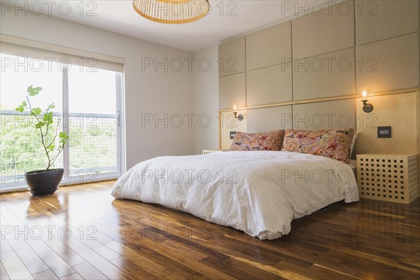 King size bed covered with white bedspread in bedroom with American walnut hardwood flooring on upstairs floor inside modern cube style home, Quebec, Canada, North America