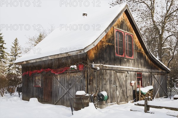 Old wooden rustic barn with red trimmed windows and Christmas decorations in winter, Quebec, Canada, North America