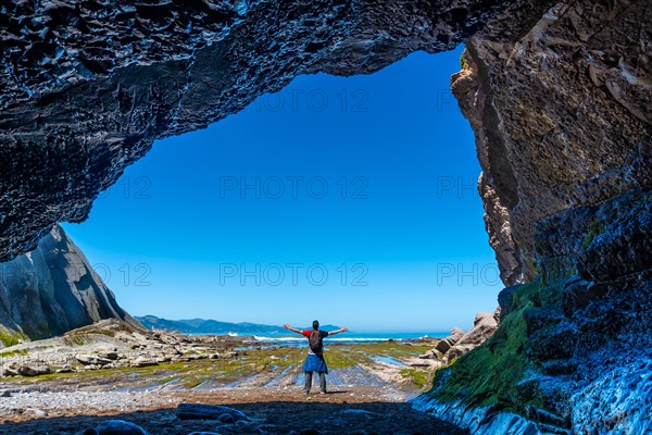 A hiker in the Algorri cove sea cave on the coast in the flysch of Zumaia, Gipuzkoa. Basque Country