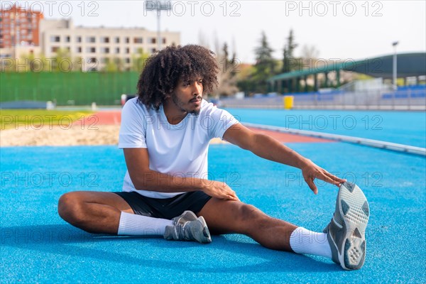 Young handsome sportive man with african hairstyle stretching in a running track