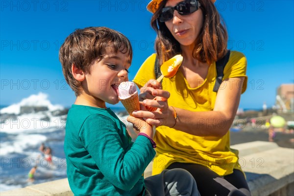 Mother with her little boy son eating ice cream by the sea on summer vacation