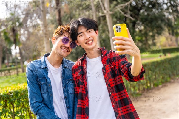 Young happy multi-ethnic gay couple taking a selfie together in a park