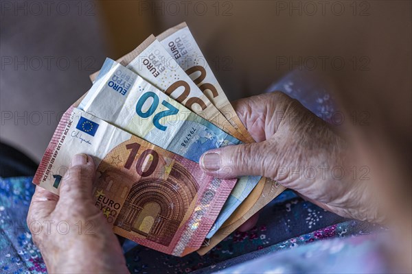 Senior citizen with wrinkled hands counts her money at home in her flat and holds banknotes in her hand, Cologne, North Rhine-Westphalia, Germany, Europe