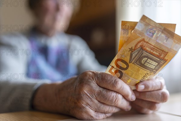 Senior citizen with wrinkled hands counts her money at home in her flat and holds banknotes in her hand, Cologne, North Rhine-Westphalia, Germany, Europe