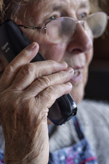 Senior citizen looks serious, frightened while talking on the phone in her living room, Cologne, North Rhine-Westphalia, Germany, Europe