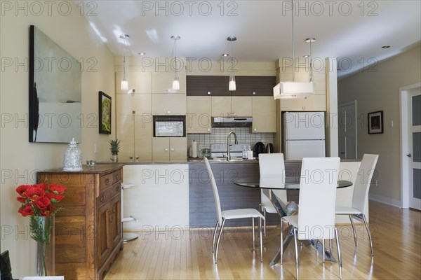 Dining room with round glass table, white leather high -back chairs and kitchen inside a renovated ground floor apartment in an old residential cottage style home, Quebec, Canada, North America