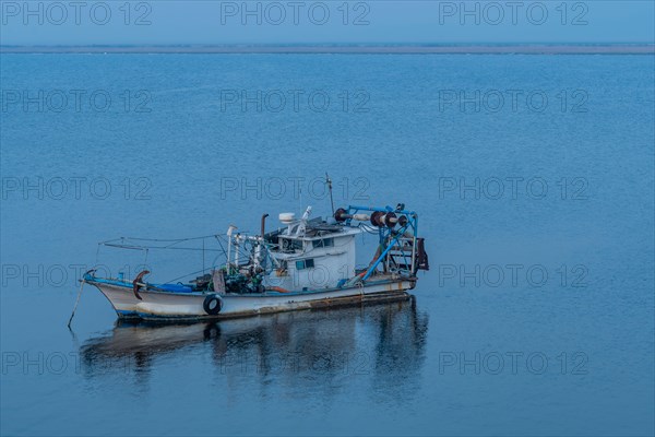 Moored white and blue fishing boat basking in the tranquil blue expanse of calm waters, in South Korea