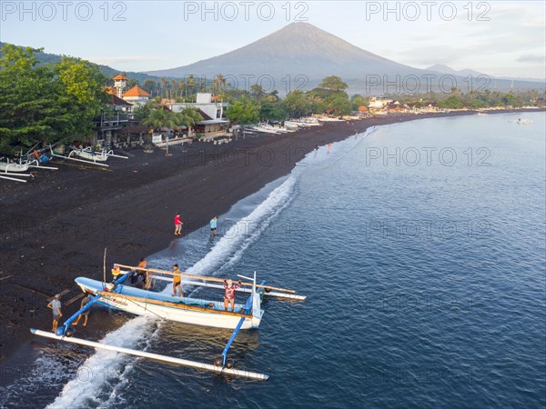 Fishermen loading fish from their outrigger boats in the morning on the black beach of Amed, Mount Agung in the background, Amed, Karangasem, Bali, Indonesia, Asia