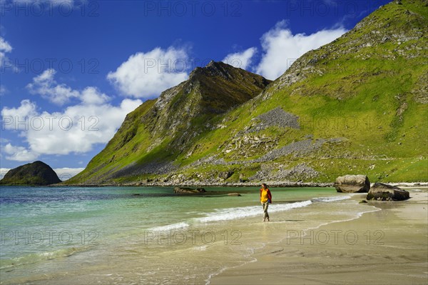 Landscape with sea at the sandy beach of Haukland (Hauklandstranda) with the mountain Veggen. A woman walks barefoot on the beach. Good weather, blue sky, a few clouds. Early summer. Haukland Beach, Haukland, Vestvagoya, Lofoten, Norway, Europe
