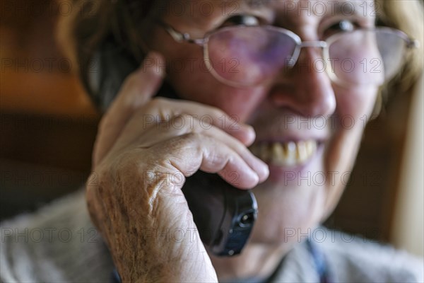 Laughing senior citizen talking on the phone at home in her living room, Cologne, North Rhine-Westphalia, Germany, Europe