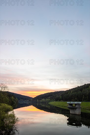 A lake in a landscape shot. A sunset and the natural surroundings are reflected in the water of the reservoir. Marbach reservoir, Odenwald, Hesse