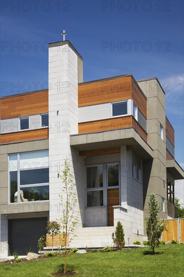 Two story grey and charcoal stone with cedar wood siding modern cube style home facade in summer, Quebec, Canada, North America