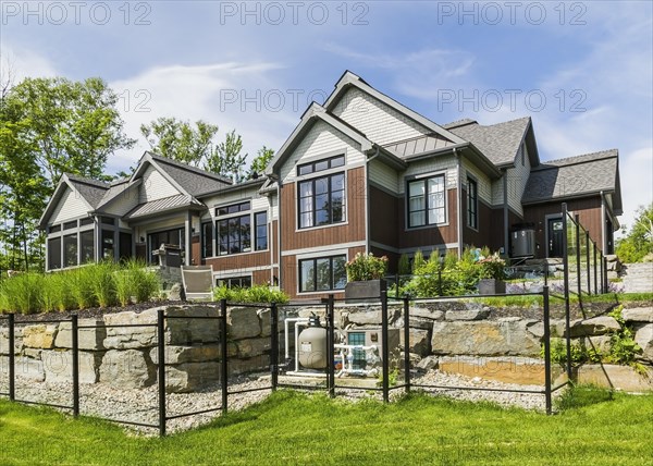 Rear view of contemporary natural stone and brown stained wood and cedar shingles clad luxurious bungalow style home in summer, Quebec, Canada, North America