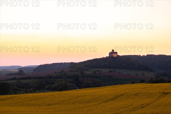 Landscape at sunrise. Beautiful morning landscape with fresh yellow rape fields in spring. Small castle in the yellow fields on a hill. Historic Ronneburg Castle in the middle of nature, Ronneburg, Hesse, Germany, Europe