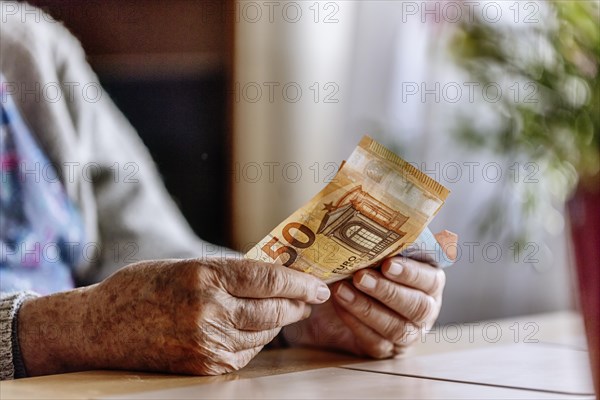 Senior citizen with wrinkled hands counts her money at home in her flat and holds banknotes in her hand, Cologne, North Rhine-Westphalia, Germany, Europe