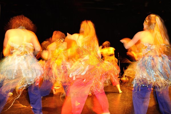 Blurry image of dancers in colorful costumes performing energetically on stage